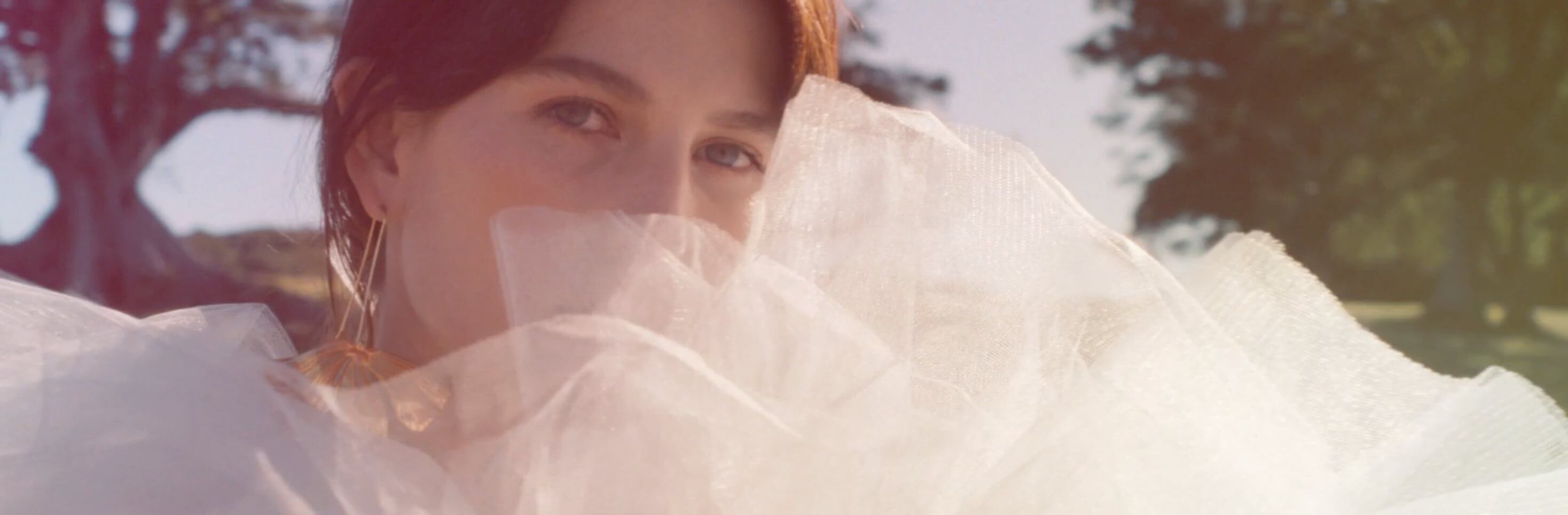 A woman gazing over soft white tulle in a park